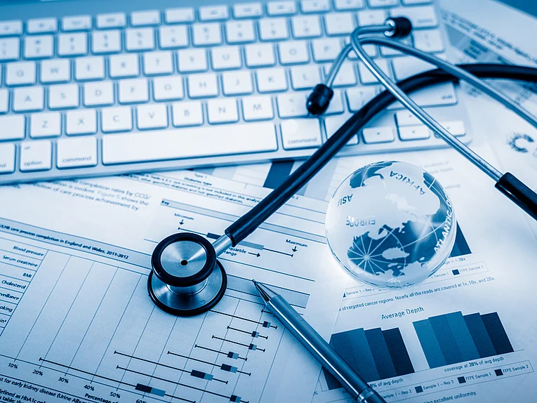 Text: "Datenmanagement für klinische Studien", im Bild zu sehen sind eine PC-Tastaur, ein Stethoskop, und Dokumente mit statistischen Auswertungen in Form von Graphiken und Tabellen